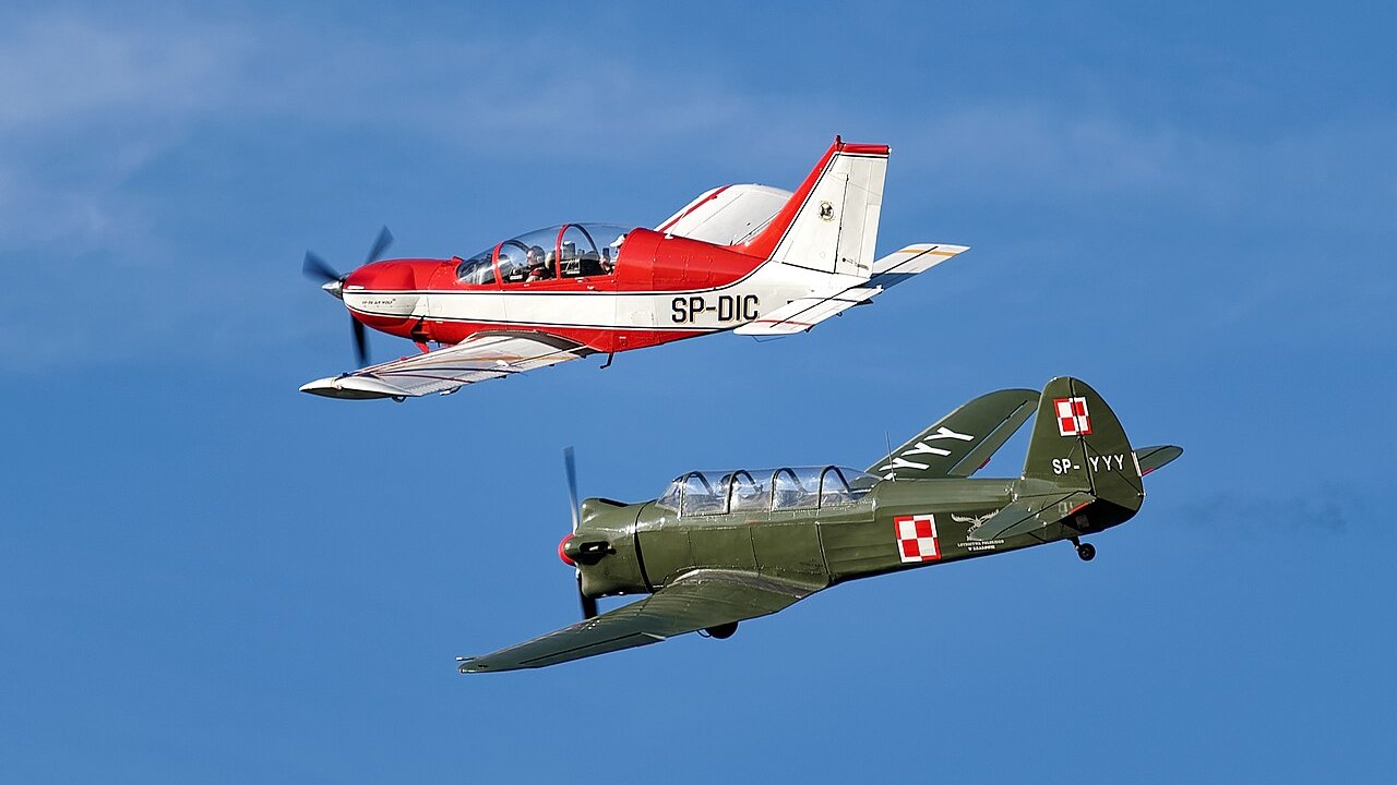 Czerwono-biały samolot PZL M-26 Iskierka SP-DIC w locie obok Jaka-18 nad Krakowem